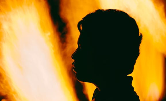 A dramatic silhouette of a person's profile against vivid orange flames.