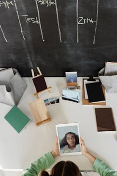 A top view of a home office desk with a video call in progress on a tablet, surrounded by books and photo frames.