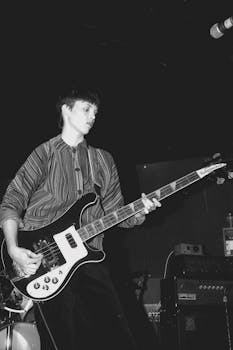 Black and white photo of a female bass guitarist performing live in the 1980s.